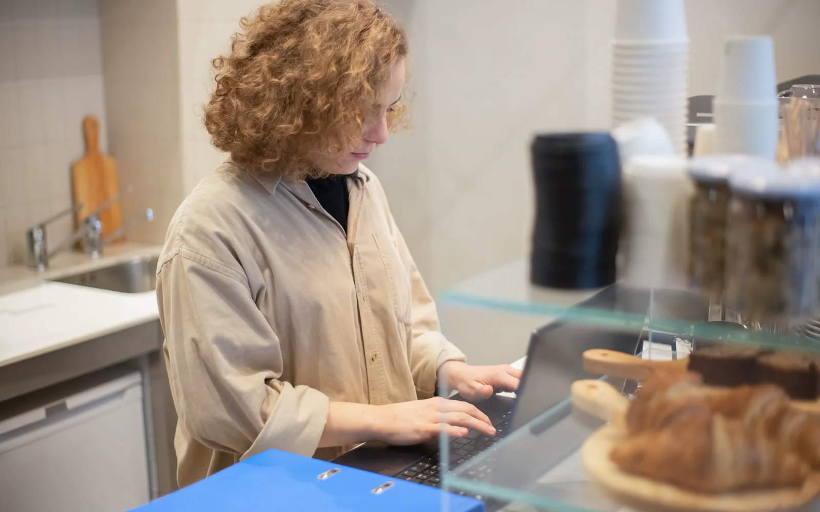 A person working at a laptop behind a bakery counter.