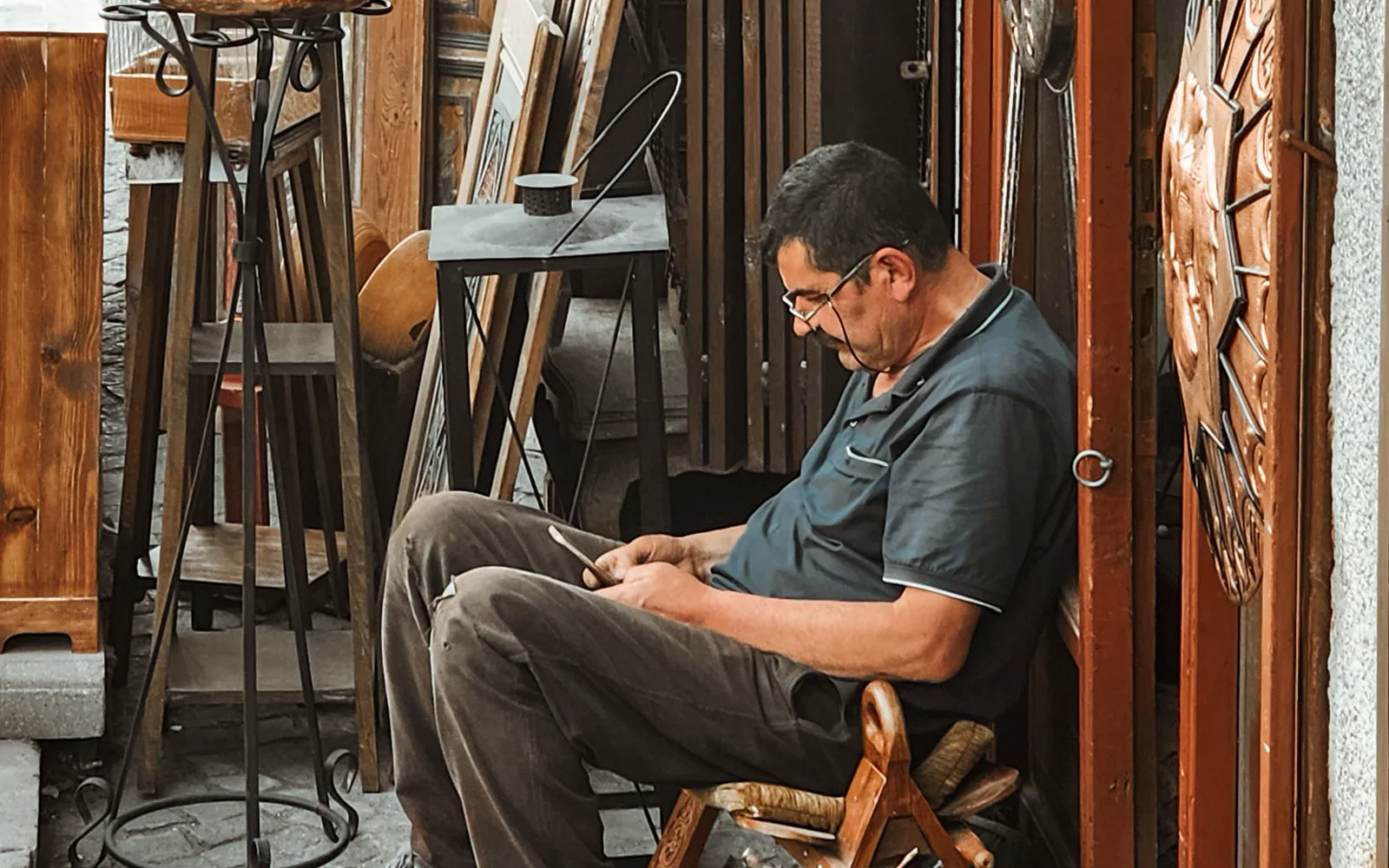 Person seated outside a craft shop, looking at a phone.