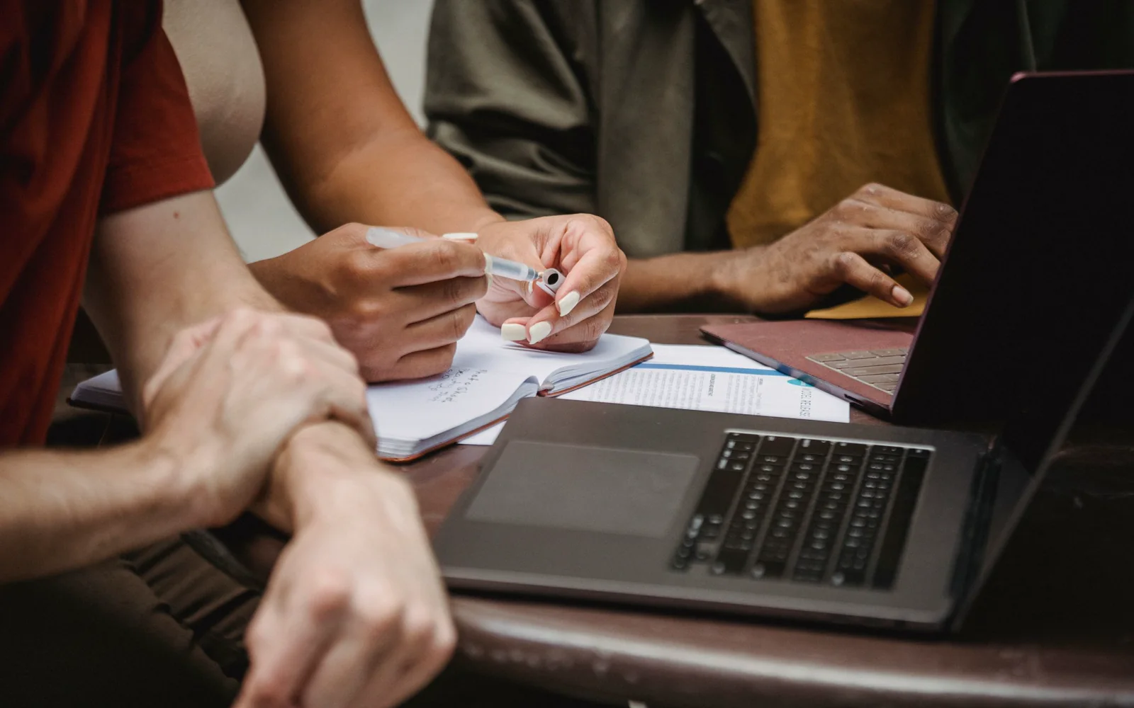 Colleagues writing notes beside open laptops during a working session.