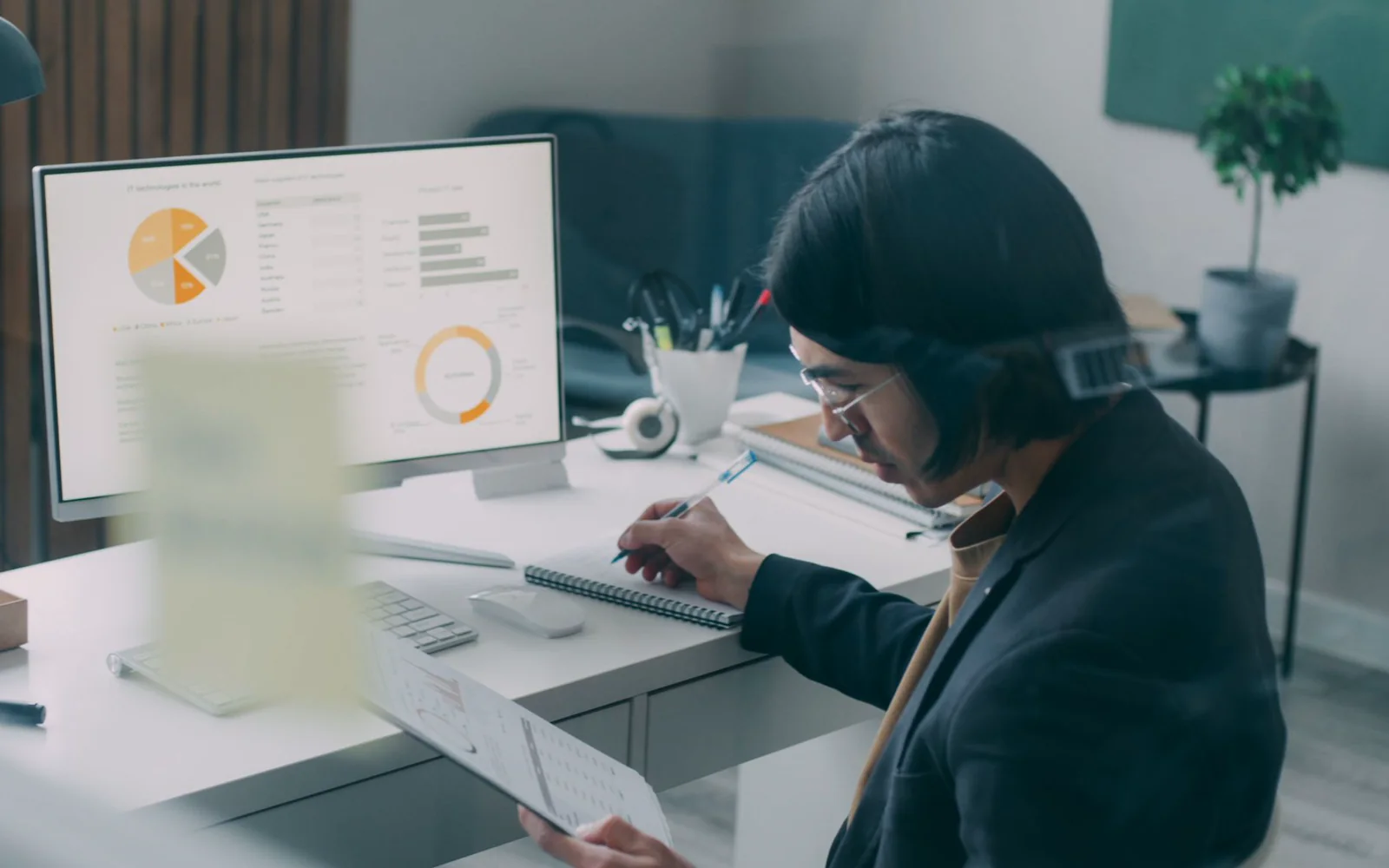 Person reviewing charts on a monitor and notes at a desk.