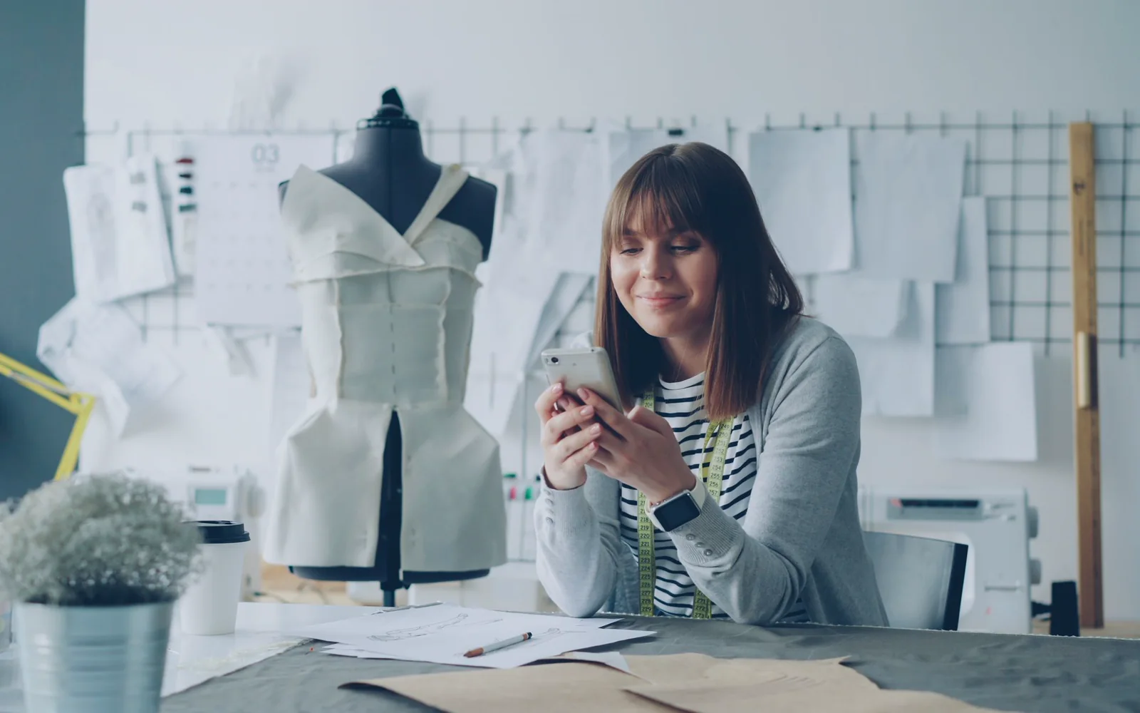 Woman using a smartphone at a table beside a dress form.